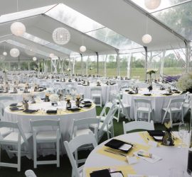 An image from within a setup clear span tent of dozens of round tables with 10+ chairs per table in a tent with no tent polls inside and transparent panels in the ceiling of the tent to allow natural light in, spacious and beautiful for an event.